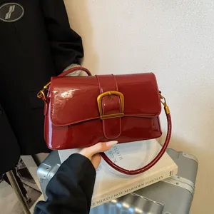 Glänzende burgunderrote Schultertasche aus Lackleder mit Goldverschluss vor City-Kulisse