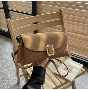 Detail of a brown suede handbag with a gold metal buckle on a light wood chair