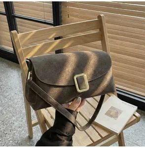 Detail of a brown suede rectangular crossbody bag with a gold buckle on a wooden chair