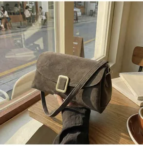 Close-up of brown suede shoulder bag with gold metal buckle in a cozy cafe setting