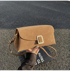 Detail view of brown faux suede satchel with gold buckle on asphalt background