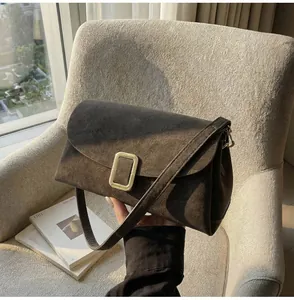 Detail of dark brown suede shoulder bag featuring a gold buckle and slim strap on a sofa