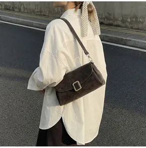 Detailed view of deep brown suede crossbody bag with vintage gold buckle on casual outfit