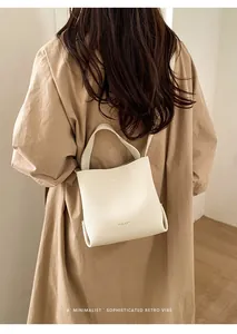Detalle del bolso tipo cubo de cuero blanco con textura de lichi llevado con gabardina beige