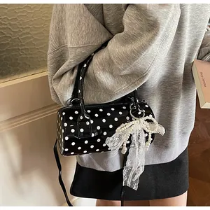 Detail of black polka dot cylinder bag featuring a large lace bow and pearl charm
