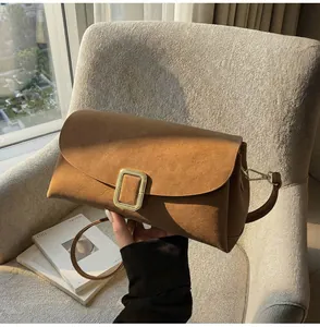 Detail of a brown suede crossbody bag with gold rectangular clasp on fabric surface