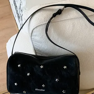 Black rivet shoulder bag with silver star studs and adjustable strap on a sofa