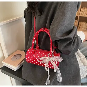 Detail of red polka dot cylinder bag with white lace bow and pearl charm pendant