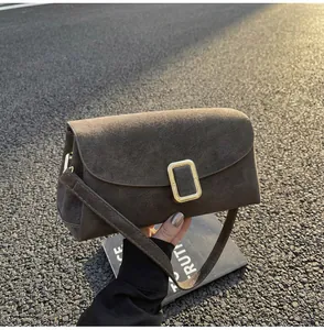 Close-up of brown suede pillow bag with a gold buckle on an urban asphalt background