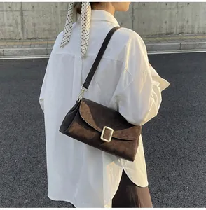 Detail of dark brown suede shoulder bag with gold clasp shown on a white shirt