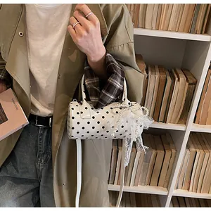 Close-up of white polka dot cylinder bag with lace pearl bow on a shoulder