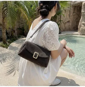 Brown suede shoulder bag with gold buckle shown on a model in a luxury resort setting