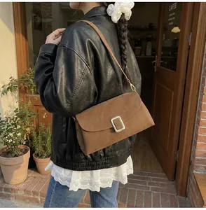 Retro brown suede shoulder bag with silver buckle worn over the shoulder by a model