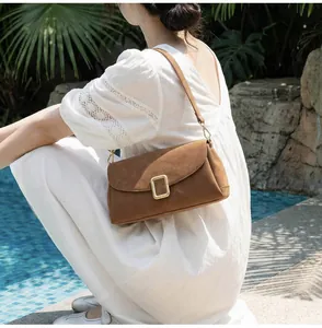 Detail of a brown suede rectangular shoulder bag with a gold rectangular metal buckle