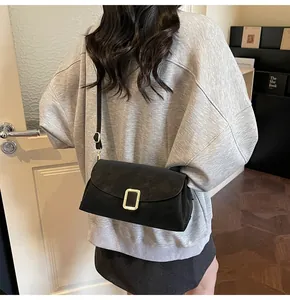 Detail of matte black crossbody bag with gold buckle on a model wearing a grey hoodie