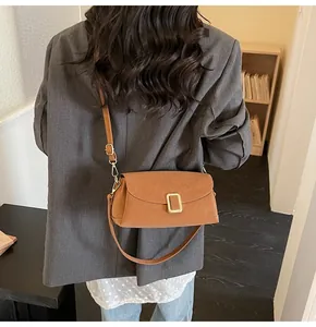 Close-up of caramel brown crossbody bag with gold buckle on a grey suit outfit