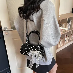 Cylindrical polka dot handbag with bow charm shown as a crossbody bag on model