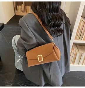 Close-up of brown leather pillow bag with gold clasp paired with a grey blazer