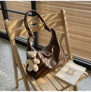 Detail of dark brown leather hobo bag on a chair with a cute teddy bear charm pendant