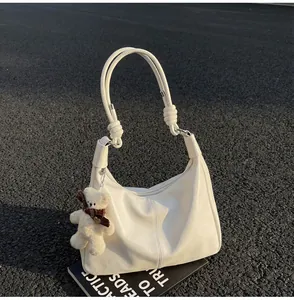 Close-up of a white leather hobo bag featuring a knotted handle and a cute plush bear charm