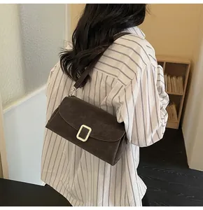 Detail view of a retro dark brown suede crossbody bag with a gold metal buckle on a model