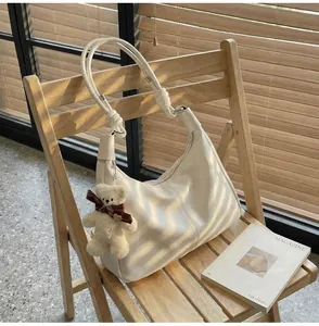 Close-up of white crescent tote bag with knot details and cute bear charm on wooden chair