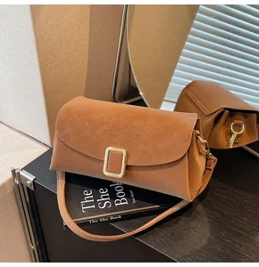 Detailed shot of brown faux suede crossbody bag with gold buckle on a book