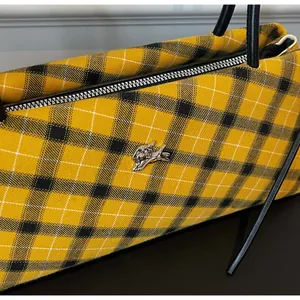 Close-up of yellow plaid fabric texture and silver dog-shaped logo on shoulder bag