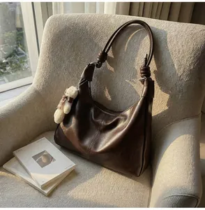 Detail of coffee brown leather tote bag with unique knotted strap on a gray sofa