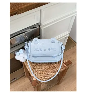 Detail of light blue cat-shaped crossbody bag with ear details and plush ball charm