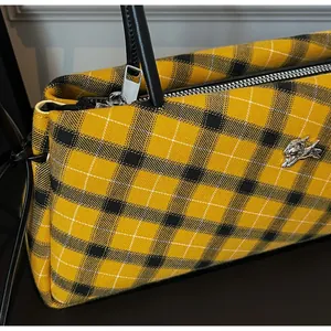 Detail of yellow checkered tweed bag with leather handle and silver metal animal logo