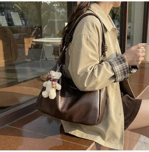 Detail of dark brown leather tote bag with unique knotted strap and bear charm