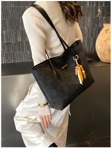 Detail of black tote bag with embossed texture, golden logo, and bohemian bead charm