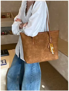 Detail of a brown suede tote bag with leather tag and decorative beaded charm