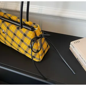 Detail of yellow plaid tote bag with slim black handles and decorative ribbon accent