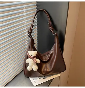 Close-up of brown faux leather hobo bag with knotted strap and plush bear charm