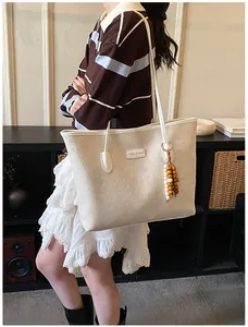 Detail of cream tote bag featuring embossed logo textures and wooden bead tassel decor