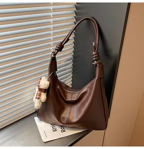 Detail of soft dark brown leather shoulder bag with decorative strap knot and bear charm