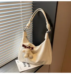 Detail of cream leather shoulder bag with cute teddy bear charm and knotted strap accent