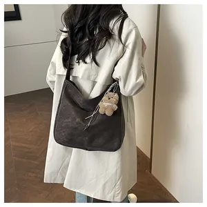 Détail du sac à bandoulière marron foncé en forme de demi-lune avec charm ours en peluche