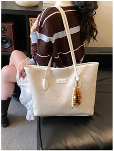 Detailed macro of white tote bag featuring embossed patterns and wood bead tassel
