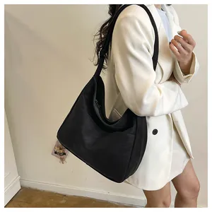 Sac fourre-tout noir minimaliste avec large bandoulière porté par un mannequin en studio