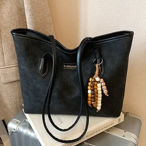 Vintage black tote bag with beaded pendant and metal logo on a metallic case