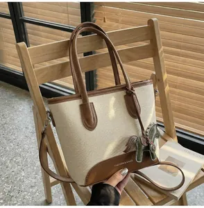 Detalle de bolso tipo cubo de lona con ribete de cuero y colgante de caballo decorativo