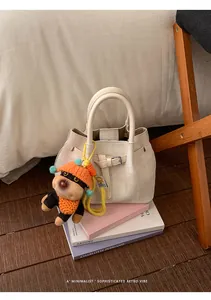 Detail of cream bucket bag with woven texture and a cute puppy plush charm on books