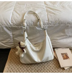 Detail of cream white half-moon shoulder bag with soft leather texture and bear charm