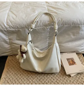 Close-up of a white leather Hobo bag with a cute teddy bear pendant on a woven mat