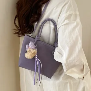 Sac bandoulière minimaliste violet mat avec breloque ours porté par un mannequin femme