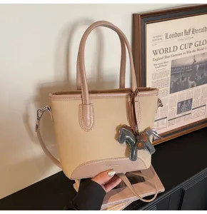 Detalle del bolso de lona beige con ribete de cuero y un colgante de poni decorativo
