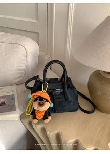 Detail of denim bucket bag with black leather handles and cute plush puppy charm